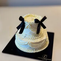 This striking two-tiered cake combines classic white piping with bold black ribbons for a timeless, monochromatic look. It's a sophisticated choice that makes a statement at any formal celebration.