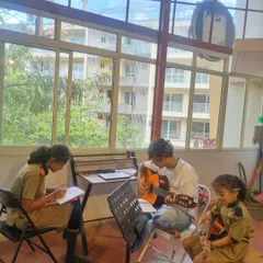 Students working together during a lesson, one writing music theory while others practice on guitar. Collaboration is key to our teaching philosophy.