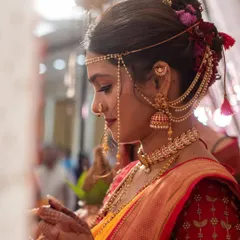 A side profile of a traditional Maharashtrian bride, highlighting the intricate floral bun hairstyle, temple jewellery, and the iconic mundavalya across the forehead.