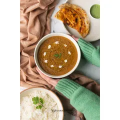A comforting bowl of Dal Makhani, presented with rice and naan. The overhead perspective and cozy styling make this a classic, heartwarming depiction of a beloved Indian dish.
