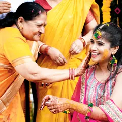 A heartwarming moment of a mother applying Haldi to the smiling bride, full of love and tradition.