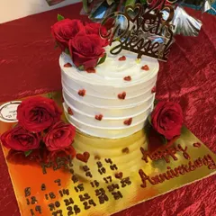 A heartfelt cake for a 25th anniversary. This design features a "25 Years Blessed" topper, fresh red roses, and a custom calendar marking the special date on the cake board.