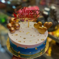 A birthday cake designed to make someone feel truly special. This creation features a beautiful blue and white gradient, adorned with golden hearts, spheres, and delicate gold leaf flakes, all topped with an elegant 'Happy Birthday' sign. I can create a similar masterpiece for your next celebration.
