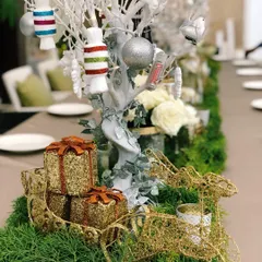 Detailed view of the Christmas centerpiece, highlighting the textures of the golden wire reindeer and sparkling gift decorations nestled in the greenery.