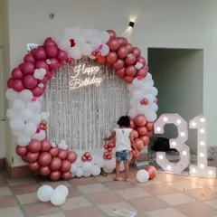 This grand backdrop for a 31st birthday includes a circular balloon arch in rose gold and white, a silver shimmer curtain for photos, a neon sign, and large light-up numbers.