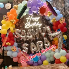 An Art Party theme is perfect for creative kids. This setup for a 7th birthday includes a rainbow balloon arch decorated with giant crayon and paintbrush cutouts, and a neon "Happy Birthday" sign.
