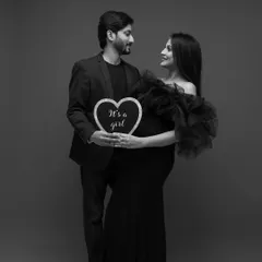A beautiful black and white portrait for a gender reveal, holding a heart-shaped sign that says "It's a girl."