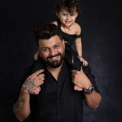 A classic father and child portrait with the little one enjoying a ride on dad's shoulders. The coordinated black outfits give this studio shot a sleek and modern look.