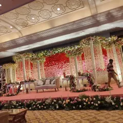 An elaborate stage decoration for a wedding reception. This design features a backdrop of red and pink flowers, hanging floral strings, and multiple columns, creating a rich and layered look.