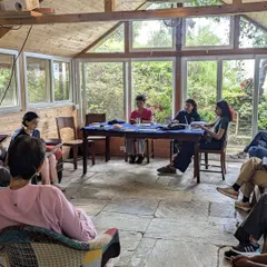 An indoor workshop in session. Participants engage in a group reading, sharing their work and offering constructive feedback in a supportive environment.