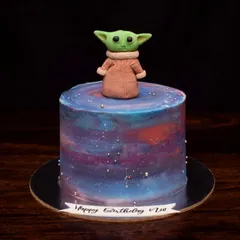 This is the way. A galaxy-themed cake featuring a hand-molded fondant Baby Yoda (Grogu) on top. The buttercream base is painted with cosmic colors to create a Star Wars cake that's out of this world.