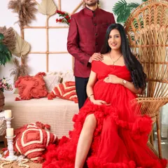 A regal portrait of the expecting couple in our boho-inspired studio. The mom-to-be is seated on a peacock chair in a vibrant red gown, creating a striking and stylish image.