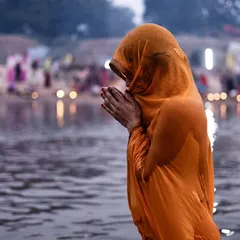 A devotee stands waist-deep in the river, her hands joined in prayer, embodying a moment of serene devotion during the Chhath Mahaparv.