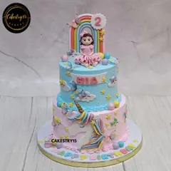 This two-tier unicorn cake is a fairytale dream. The choco-vanilla cake features a sweet girl figurine under a rainbow on top, with a 2D unicorn, butterflies, and stars decorating the pink and blue tiers.