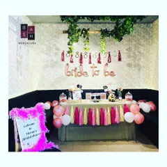 This is the full view of a bridal shower welcome area and decor table. A personalized sign greets guests, leading them to a decorated space with balloons, tassels, and props for the celebration.