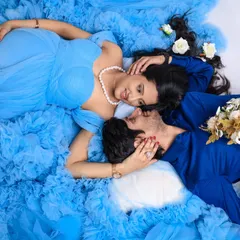 An artistic top-down shot of an expecting couple sharing an intimate gaze. The sea of blue tulle from the maternity gown creates a beautiful, dreamy texture around them.
