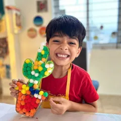 This young man's smile says it all. He's so proud of his colorful cactus made from pom-poms, a fun and tactile craft that's perfect for developing fine motor skills.