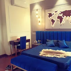 A striking modern bedroom centered around a royal blue velvet bed. The design includes a matching tufted bench, a minimalist study desk, and a custom backlit world map art piece on the wall, creating a bold and personalized travel-themed sanctuary.