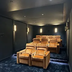 A different perspective of the classic theater room with tiered seating. The warm wall sconces provide soft, ambient lighting that enhances the cinematic feel without causing any glare on the screen.