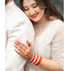 A close-up on the bride's radiant smile and beautiful henna, as she rests her head on her partner's shoulder.