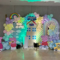 A playful Peppa Pig theme for a 4th birthday celebration. This large-scale setup features multiple backdrops creating a Peppa Pig world, character standees, a rainbow balloon, and a 'Happy Birthday' neon sign.