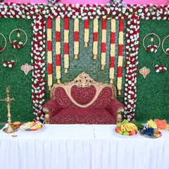 A full view of a traditional baby shower stage. The setup includes the main backdrop, a decorated table for offerings, and a royal red sofa for the parents-to-be.