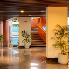 The entrance lobby of the Sona Vistaas Clubhouse, where polished marble floors reflect the warm light and greenery. This view offers a glimpse of the central staircase in the background, hinting at the dynamic spaces that unfold within.