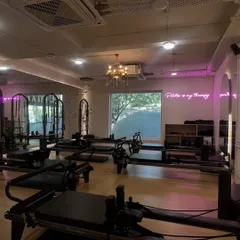 A wide view of our studio, showing the lineup of reformers ready for a class. The combination of natural light and our signature pink neon glow creates the perfect atmosphere to work out in.
