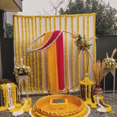 For this Haldi ceremony, I designed a setup that blends tradition with modern elegance. The backdrop features strings of vibrant marigolds, while the seating area is defined by a beautiful urli, all framed by a contemporary golden ring draped in rani pink and yellow fabric.