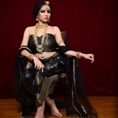 A powerful pose in the black and gold dhoti-saree, showcasing the intricate gold patterns and the off-shoulder blouse. This outfit is paired with our traditional gold temple jewellery.