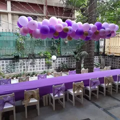 An outdoor dining setup for a kids' party, with a long purple balloon garland suspended over the table.