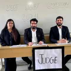 As a judge for the semi-finals of an Intra Moot Court Competition. The handwritten "Judge" sign shows the raw, authentic environment of these student-run events, where the passion for law is truly visible.
