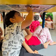 We believe in making learning interesting by changing the environment. Here, a child is completely absorbed in coloring under a table, a simple twist that turns a familiar activity into a new and exciting exploration.