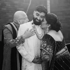 A groom receiving a hug and a kiss from his parents. This black and white photo is full of warmth and emotion, a memory to be treasured forever.
