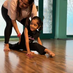 I believe in giving each child personal attention to ensure they learn safely and correctly. Here, I'm helping one of my students with her splits, celebrating her progress with a smile.