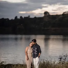 A serene and moody portrait of Prem and Jinal by a lake at dusk. The dramatic sky and calm water create a beautiful, cinematic backdrop for their quiet moment of togetherness.
