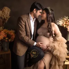 This wider shot shows the full studio setup with rustic crates and floral arrangements, which complement the earthy tones of the couple's attire for their maternity photoshoot.