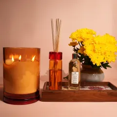 A vibrant scene featuring our three-wick candle and reed diffuser set against a backdrop of bright yellow flowers. This image perfectly captures the energy and warmth our fragrances can bring to a room.