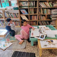 Two children are deeply engrossed in their research, surrounded by a wealth of books and reference materials. Our well-stocked library is a cornerstone of the environment, supporting their independent investigations.