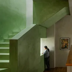 A monolithic staircase finished in a serene green oxide plaster creates a powerful play of form, light, and shadow. We use bold, continuous material applications like this to define volumes and create a tranquil, immersive experience within the home.