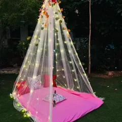 A dreamy cabana tent setup on a lawn for a unique outdoor celebration. I use a sheer canopy draped with fairy lights and floral vines to create a cozy and intimate space for you and your partner.