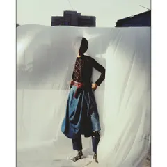 A full-body shot from a series featured in PhotoVogue, captured on 35mm film. The model, styled in Levi's, stands against a draped white sheet, creating a raw, high-contrast image that plays with shadow and form.