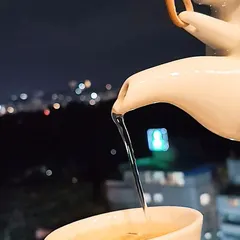 A simple, beautiful moment. Enjoy a cup of our fragrant jasmine tea being poured, with the soft, blurred lights of the Bangalore cityscape creating a serene and peaceful backdrop for your evening.