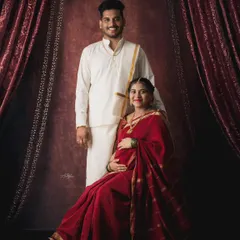 A classic portrait of a couple in traditional South Indian attire. The studio setup with rich, dark curtains creates a formal and timeless feel for this maternity photo.