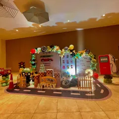 A dynamic car-themed setup for Avyaan's "two fast" second birthday. This party features a road-themed floor mat, a gas station prop, and a custom backdrop, creating a fun raceway environment.
