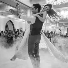A couple shares their first dance, surrounded by a cloud of dry ice. This dramatic black and white photo captures the romance and cinematic quality of a sangeet night performance.