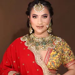 A beautiful Kundan set with green stone detailing, paired with a red and yellow lehenga. The set includes a choker, earrings, and a maang tikka.