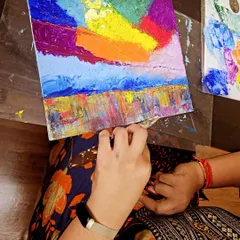 A close-up of a student creating a vibrant, multi-layered sky with a palette knife. It's a very satisfying and therapeutic process.