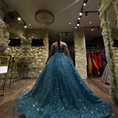 A client trying on a magnificent teal-blue sparkling ball gown. This back view shows the incredible volume and shimmer of the dress against our flower wall.