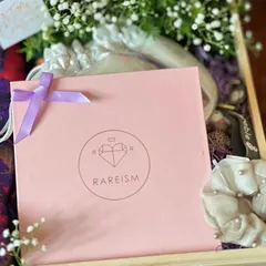 A close-up of an engagement hamper, showing the branded gift bag, a pearl scrunchie, and fresh baby's breath flowers. I focus on combining textures and high-quality items.